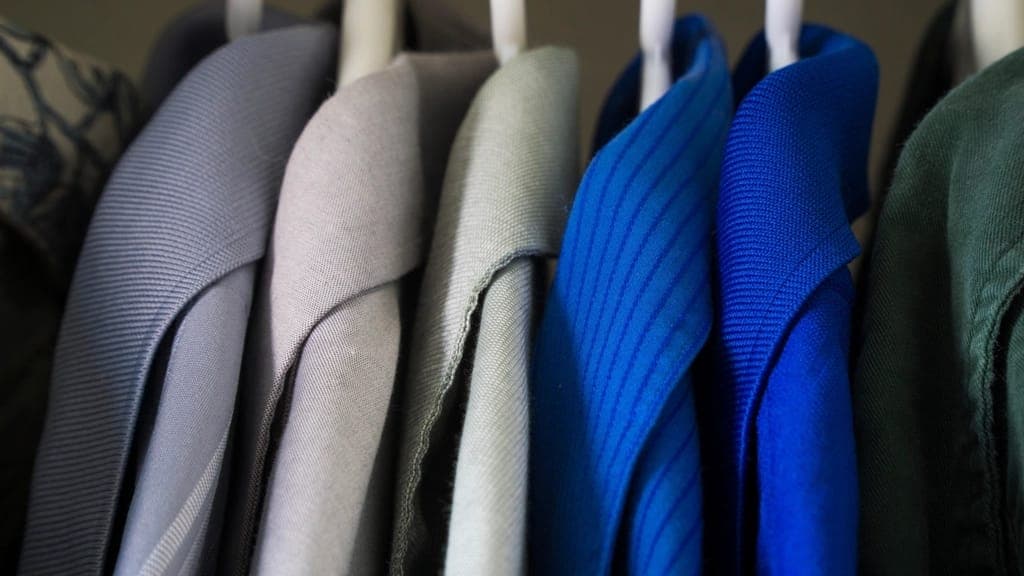 Fileira de blazers pendurados em cabides, em tons de cinza, azul e verde