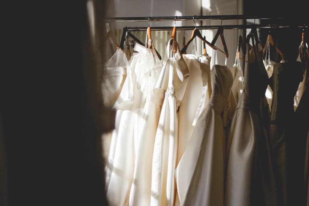 Vestidos claros de tecido fluido pendurados em cabides numa arara, em luz lateral