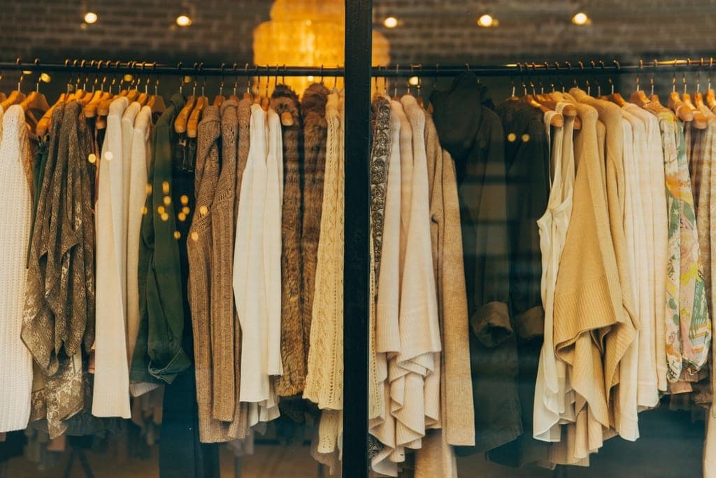 Arara de boutique com cardigãs e blusas de tons terrosos e creme, sob lâmpadas pendentes
