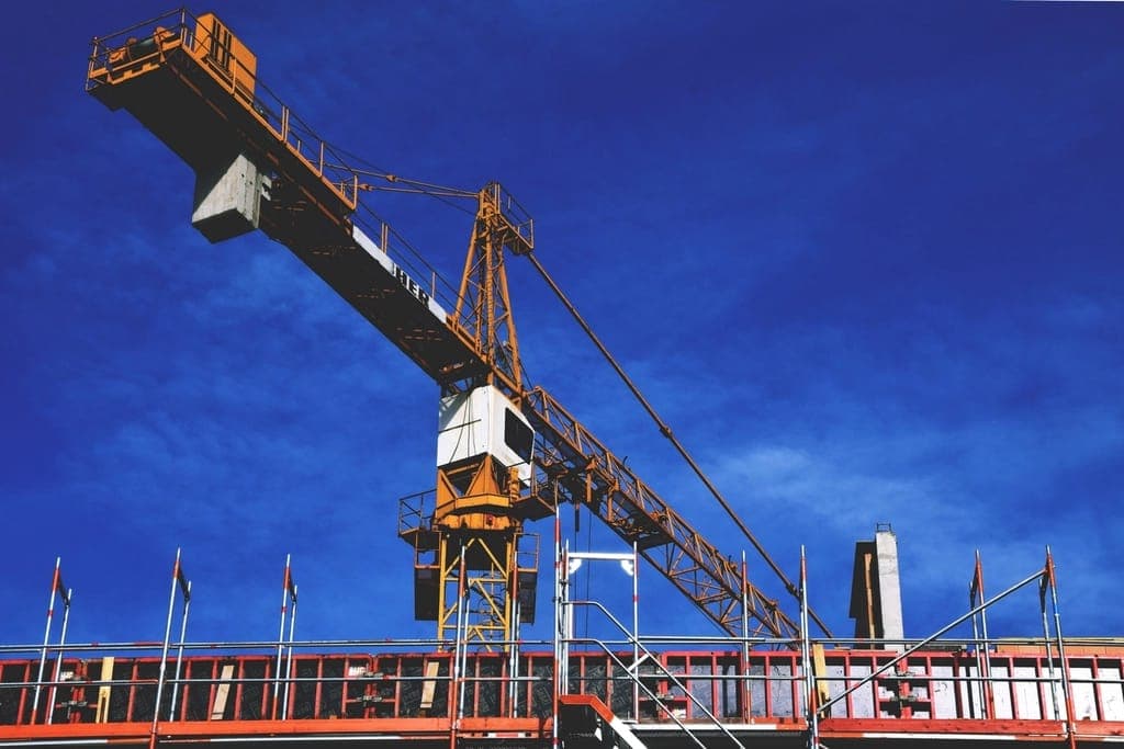 Grua amarela sobre a estrutura de um prédio em obra, com céu azul