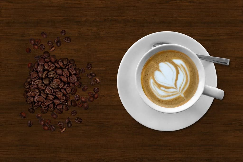 Xícara de café com desenho na espuma ao lado de um punhado de grãos torrados