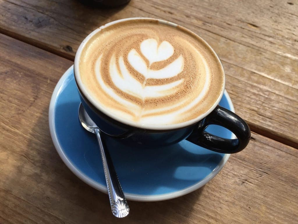 Xícara de café com desenho na espuma sobre pires azul, numa mesa de madeira