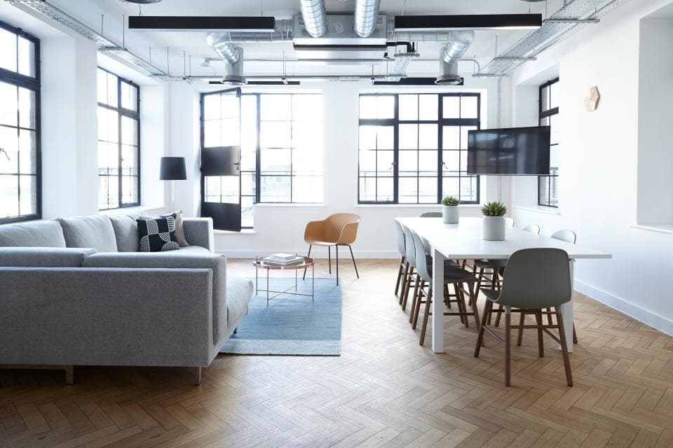 Sala ampla com janelas de caixilho preto, sofá claro e mesa de jantar