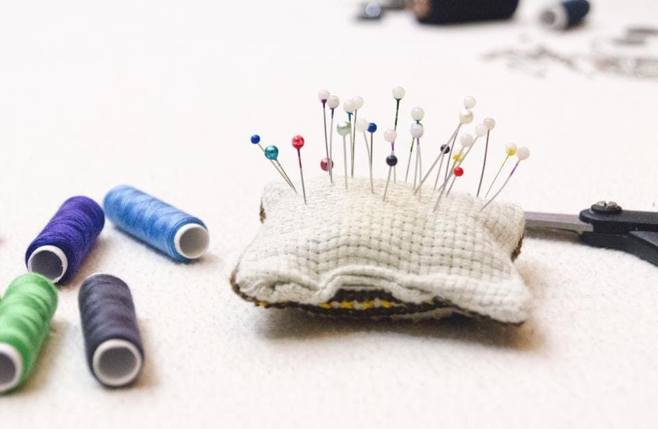 Almofada de alfinetes com alfinetes coloridos e carretéis de linha sobre uma superfície clara
