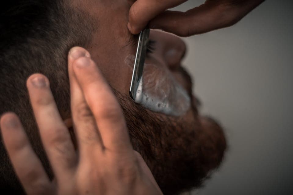 Mão esticando a pele enquanto a navalha desliza sobre a barba